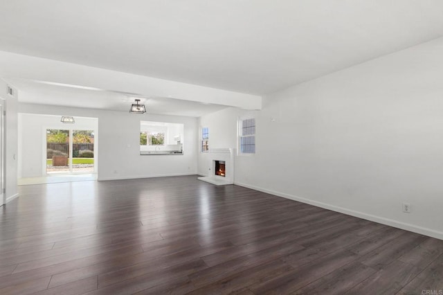 unfurnished living room featuring dark wood finished floors, a lit fireplace, and baseboards