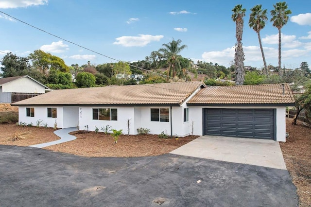 ranch-style house featuring a garage, concrete driveway, a tile roof, and stucco siding