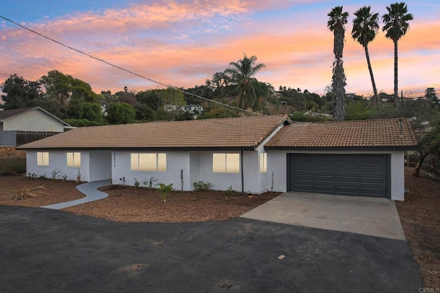 single story home with concrete driveway, a tile roof, an attached garage, and stucco siding