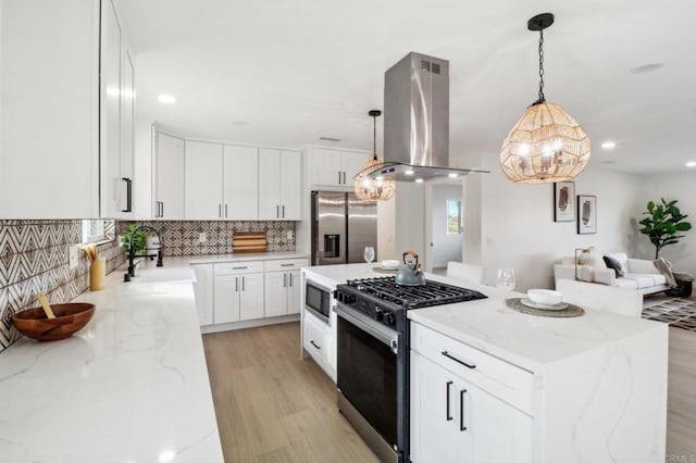 kitchen with island exhaust hood, tasteful backsplash, appliances with stainless steel finishes, white cabinetry, and a sink