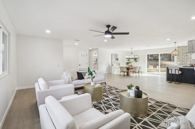 living area with baseboards, ceiling fan with notable chandelier, wood finished floors, and recessed lighting