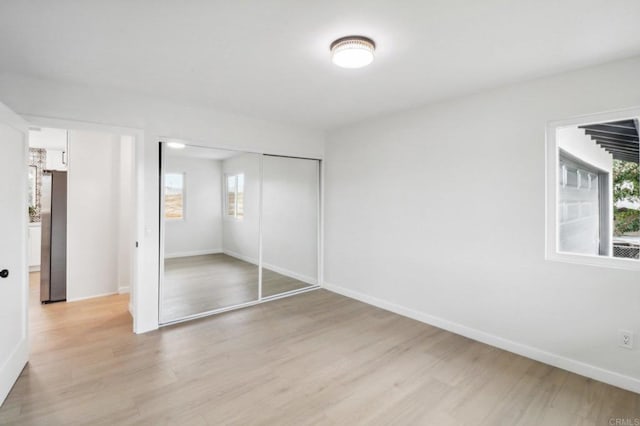 unfurnished bedroom with light wood finished floors, baseboards, and a closet