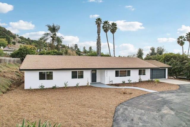 ranch-style home featuring an attached garage, stucco siding, driveway, and a tiled roof