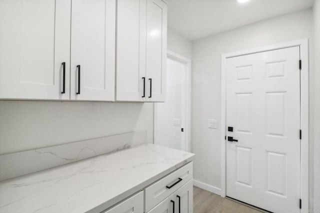 interior space with light stone countertops, baseboards, white cabinetry, and light wood finished floors