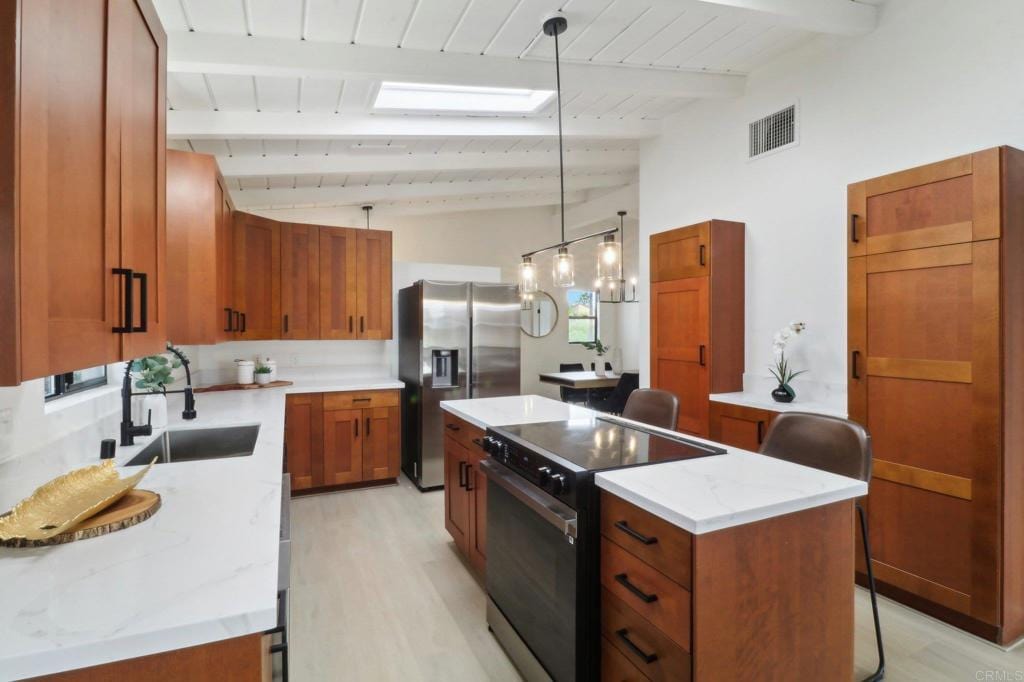 kitchen with stainless steel refrigerator with ice dispenser, visible vents, a kitchen island, a sink, and black / electric stove