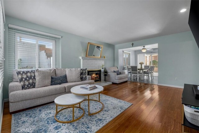 living area featuring a ceiling fan, a fireplace, baseboards, and wood finished floors