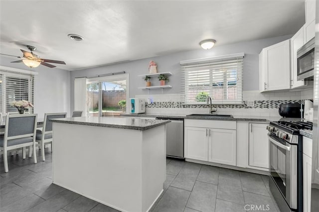 kitchen featuring a sink, a center island, appliances with stainless steel finishes, decorative backsplash, and dark stone counters