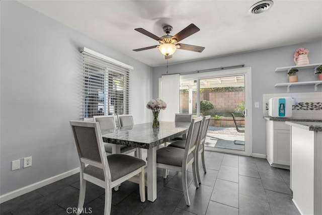 dining space with dark tile patterned flooring, visible vents, ceiling fan, and baseboards