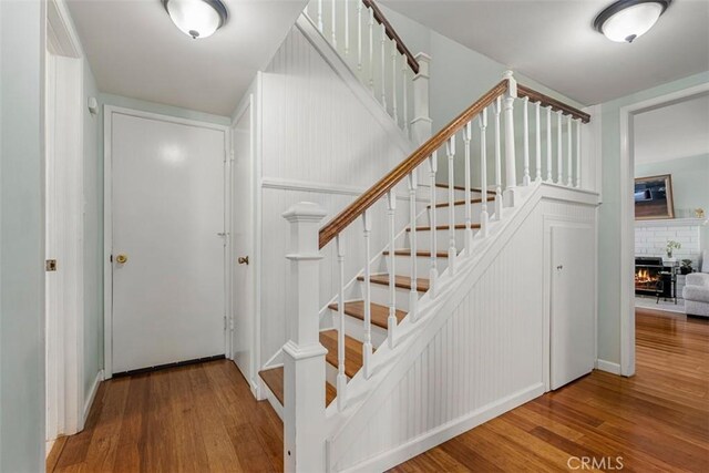 stairway with a brick fireplace and wood finished floors