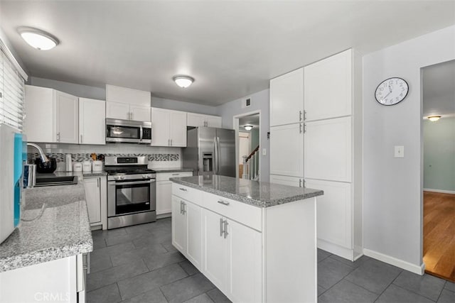 kitchen with stainless steel appliances, a sink, white cabinetry, decorative backsplash, and a center island