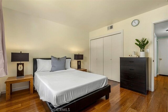 bedroom with a closet, wood finished floors, visible vents, and baseboards