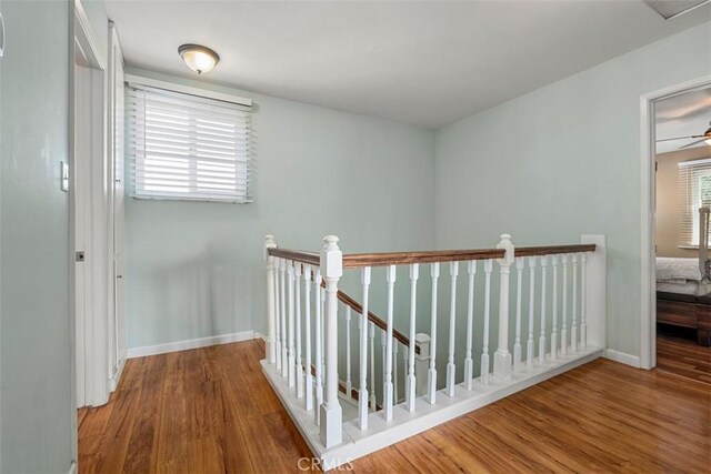 hall featuring baseboards, wood finished floors, and an upstairs landing