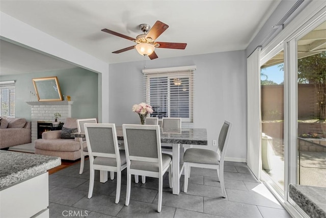 dining room with a ceiling fan, tile patterned flooring, a brick fireplace, and baseboards