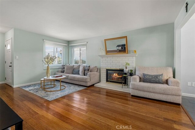 living room featuring a fireplace, baseboards, and wood finished floors