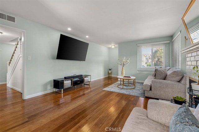 living room featuring stairway, baseboards, visible vents, and wood finished floors