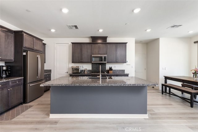 kitchen with stainless steel appliances, dark stone counters, visible vents, and dark brown cabinetry