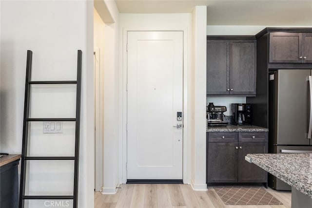 kitchen with light wood-type flooring, light stone counters, dark brown cabinets, and freestanding refrigerator