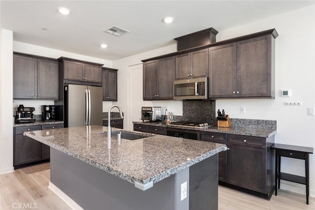 kitchen with stainless steel appliances, visible vents, stone countertops, a sink, and dark brown cabinetry