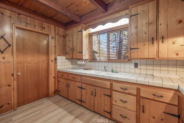 kitchen featuring light wood finished floors, wooden ceiling, backsplash, a sink, and beam ceiling