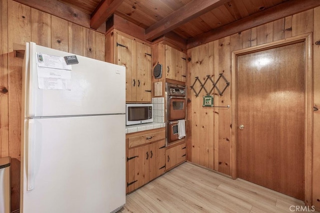 kitchen with light wood-type flooring, wooden walls, tile counters, and freestanding refrigerator