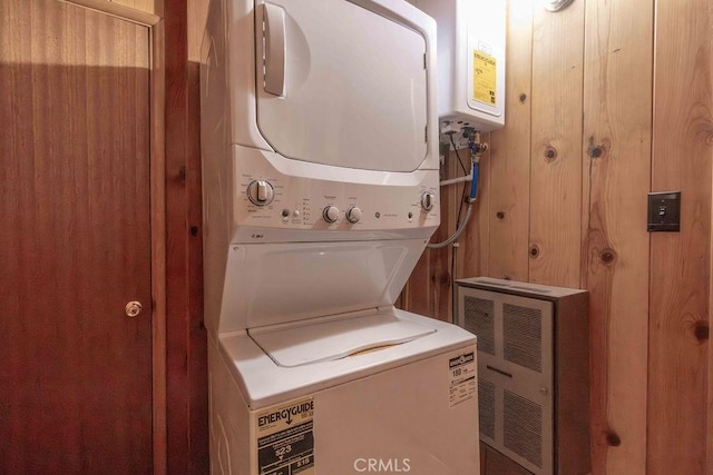 washroom with stacked washer and dryer, tankless water heater, and wood walls