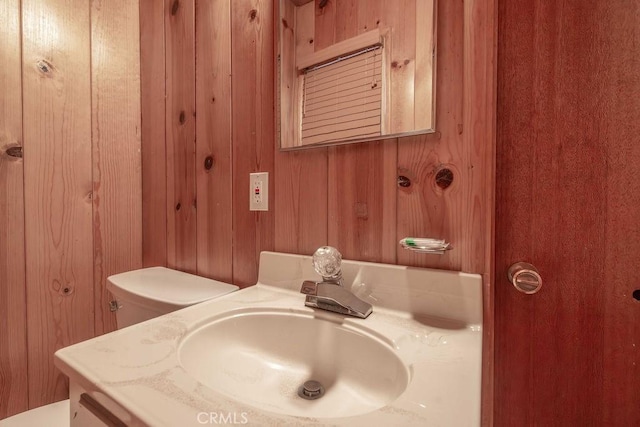 bathroom featuring toilet, wooden walls, and vanity