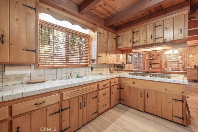 kitchen featuring decorative backsplash, a peninsula, a sink, stainless steel gas cooktop, and beam ceiling