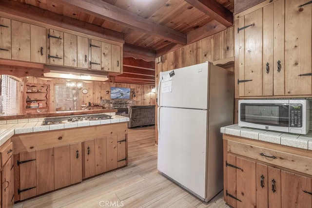 kitchen featuring tile countertops, stainless steel gas cooktop, wood walls, beam ceiling, and freestanding refrigerator