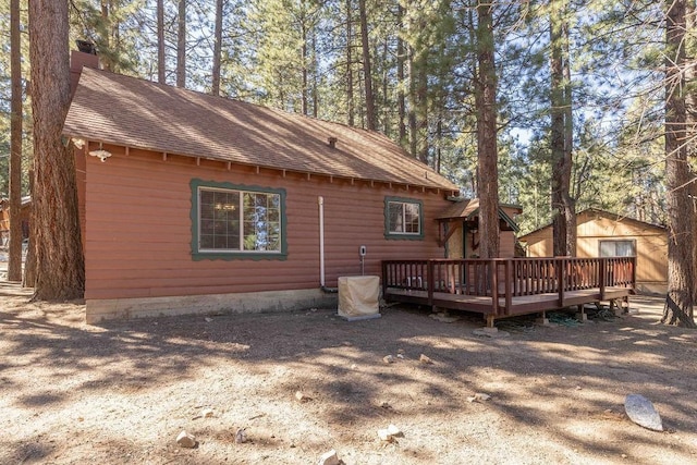 rear view of property featuring a deck, a shingled roof, and a chimney