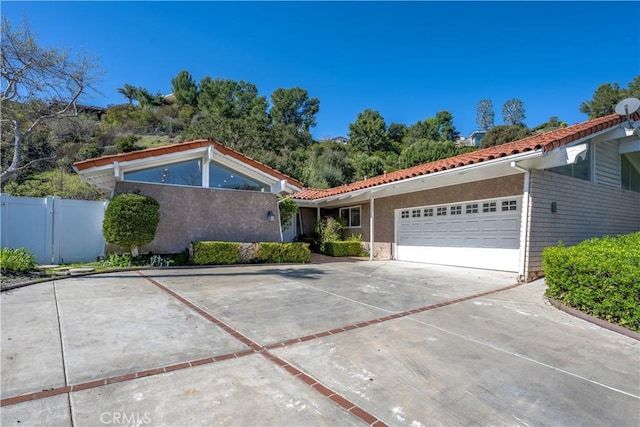 view of front of property featuring a garage, fence, driveway, a tiled roof, and stucco siding