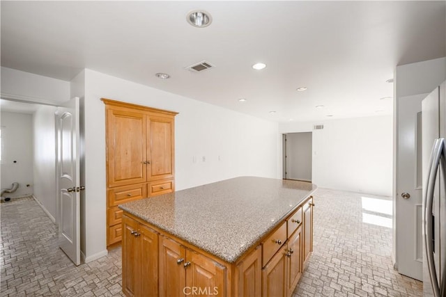 kitchen featuring light stone counters, a center island, recessed lighting, visible vents, and freestanding refrigerator