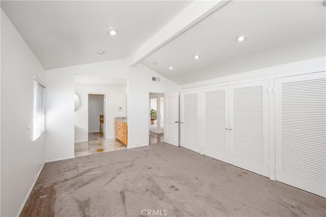 unfurnished bedroom with visible vents, light colored carpet, lofted ceiling with beams, ensuite bath, and two closets