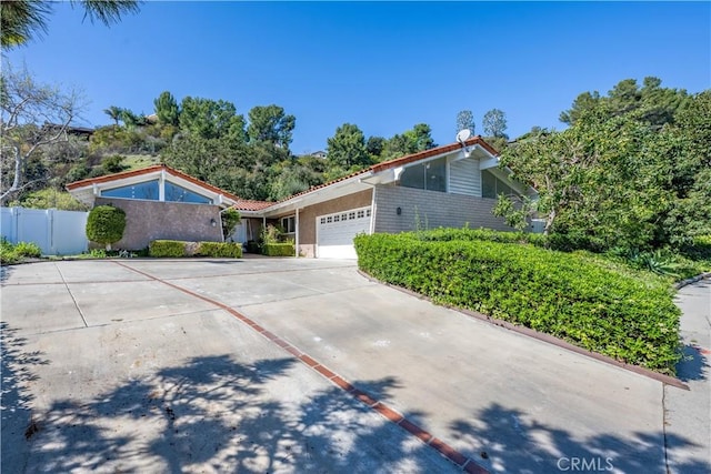 view of front facade featuring concrete driveway, brick siding, fence, and an attached garage