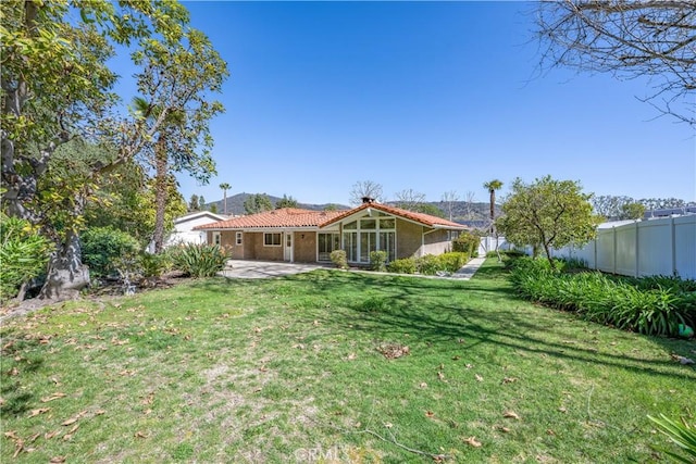 rear view of house featuring a tile roof, stucco siding, a lawn, a patio area, and fence