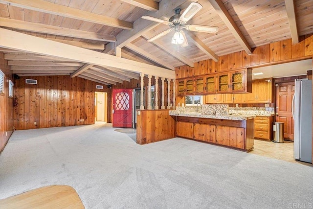 kitchen featuring freestanding refrigerator, light colored carpet, vaulted ceiling with beams, open floor plan, and wooden walls