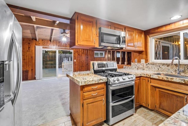 kitchen featuring a sink, ceiling fan, wooden walls, brown cabinets, and stainless steel appliances