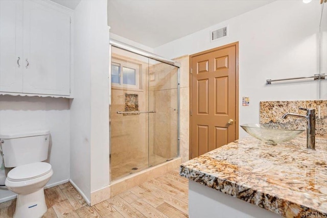bathroom featuring vanity, visible vents, toilet, wood finished floors, and a stall shower
