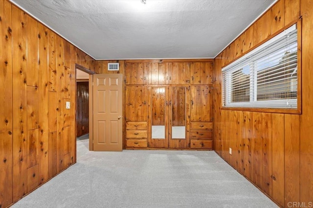 carpeted empty room with wooden walls, visible vents, and a textured ceiling