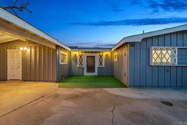 view of exterior entry with board and batten siding and a patio area