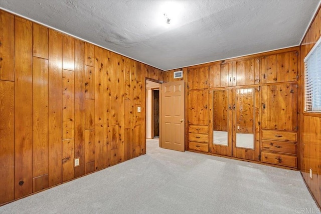 unfurnished bedroom with wood walls, carpet flooring, visible vents, and a textured ceiling