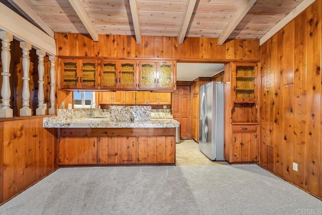kitchen with wooden walls, a peninsula, freestanding refrigerator, and beam ceiling