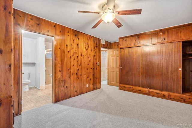 unfurnished bedroom featuring ceiling fan, a closet, ensuite bath, carpet floors, and wooden walls