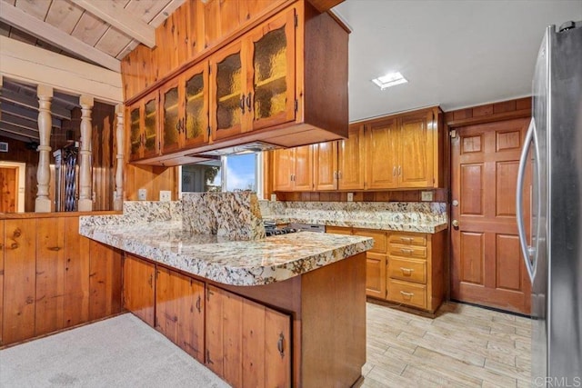 kitchen with tasteful backsplash, a peninsula, freestanding refrigerator, and wooden walls
