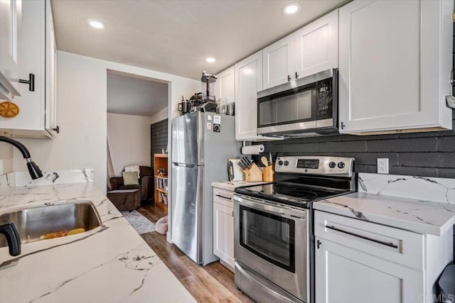 kitchen with light wood-style flooring, stainless steel appliances, a sink, white cabinets, and light stone countertops