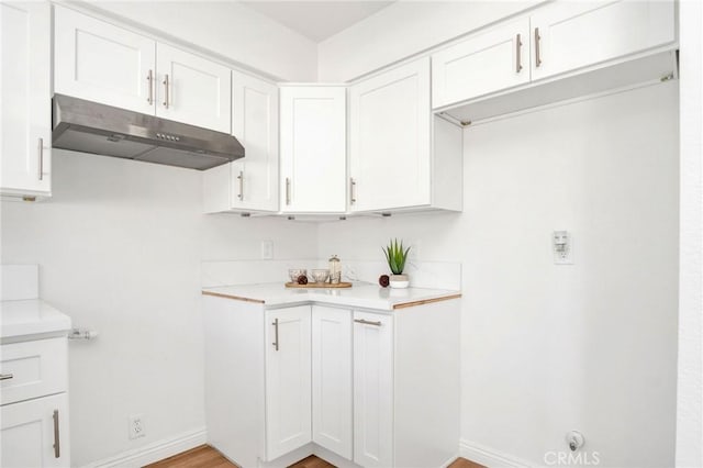 kitchen featuring baseboards, light countertops, white cabinetry, and under cabinet range hood