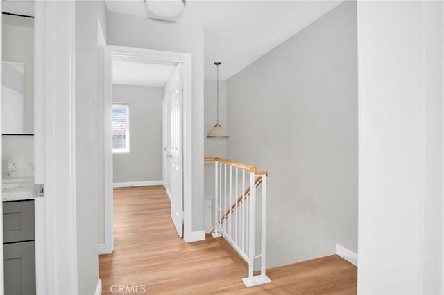 hall with light wood-style floors, baseboards, and an upstairs landing