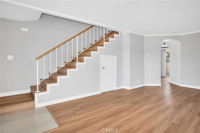 staircase with arched walkways, crown molding, wood finished floors, and baseboards