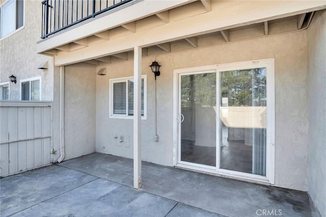 doorway to property featuring stucco siding, a patio, a balcony, and fence