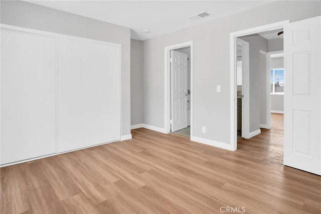 unfurnished bedroom featuring light wood-style flooring, a closet, visible vents, and baseboards