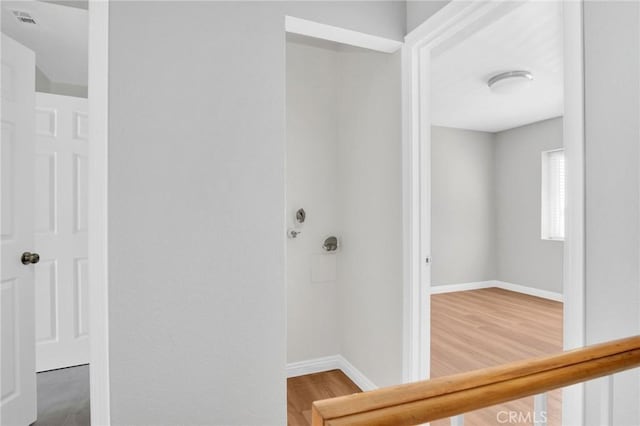 hall featuring visible vents, baseboards, and wood finished floors